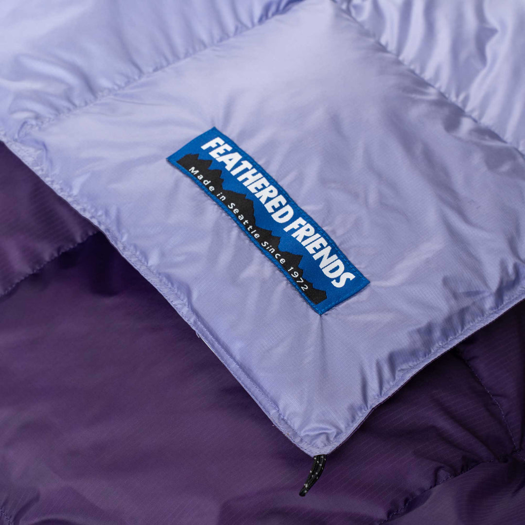Close up logo view of light purple and purple Feathered Friends down blanket