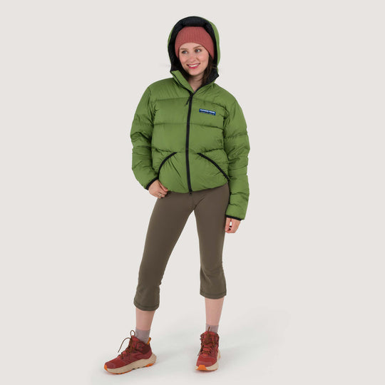 Studio front view of a woman wearing a Lichen green Feathered Friends Hooded Helios down puffer jacket