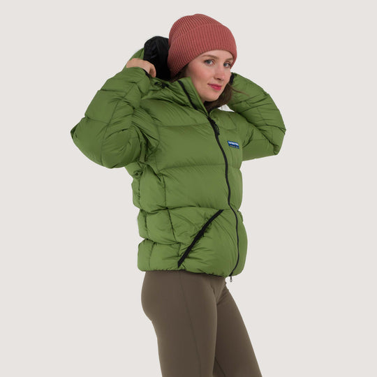 Studio side view of a woman wearing a Lichen green Feathered Friends Hooded Helios down puffer jacket