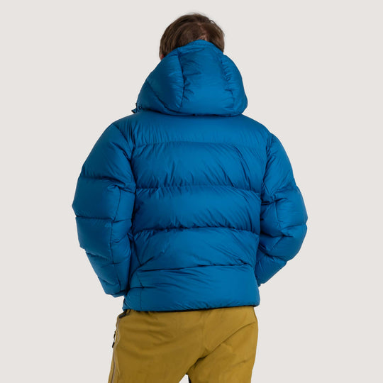 Studio back view of a man wearing a blue Feathered Friends Hooded Helios down puffer jacket