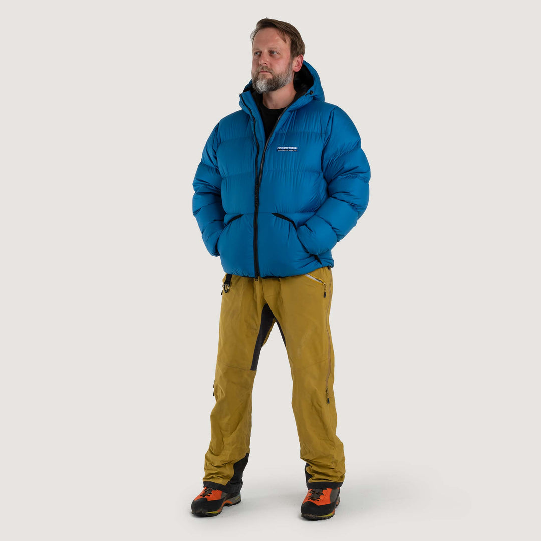Studio front view of a man wearing a blue Feathered Friends Hooded Helios down puffer jacket