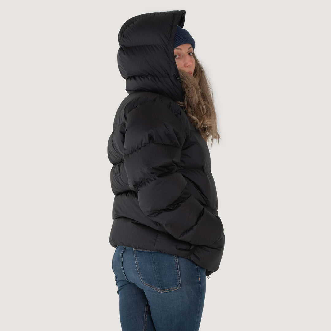 Studio back view of a woman wearing a black Feathered Friends Hooded Helios down puffer jacket