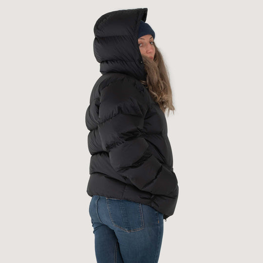 Studio back view of a woman wearing a black Feathered Friends Hooded Helios down puffer jacket