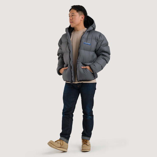 Studio front view of a man wearing a cinder gray Feathered Friends Hooded Helios down puffer jacket