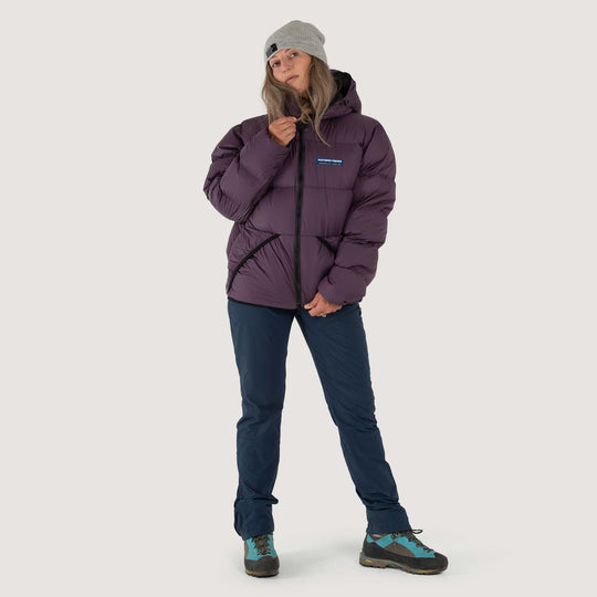 Studio front view of a woman wearing a nightshade purple Feathered Friends Hooded Helios down puffer jacket