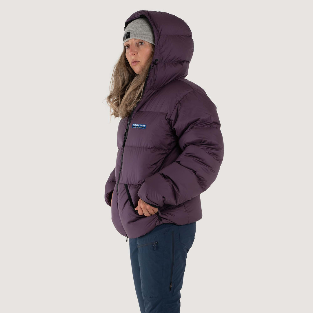 Studio front view of a woman wearing a nightshade purple Feathered Friends Hooded Helios down puffer jacket