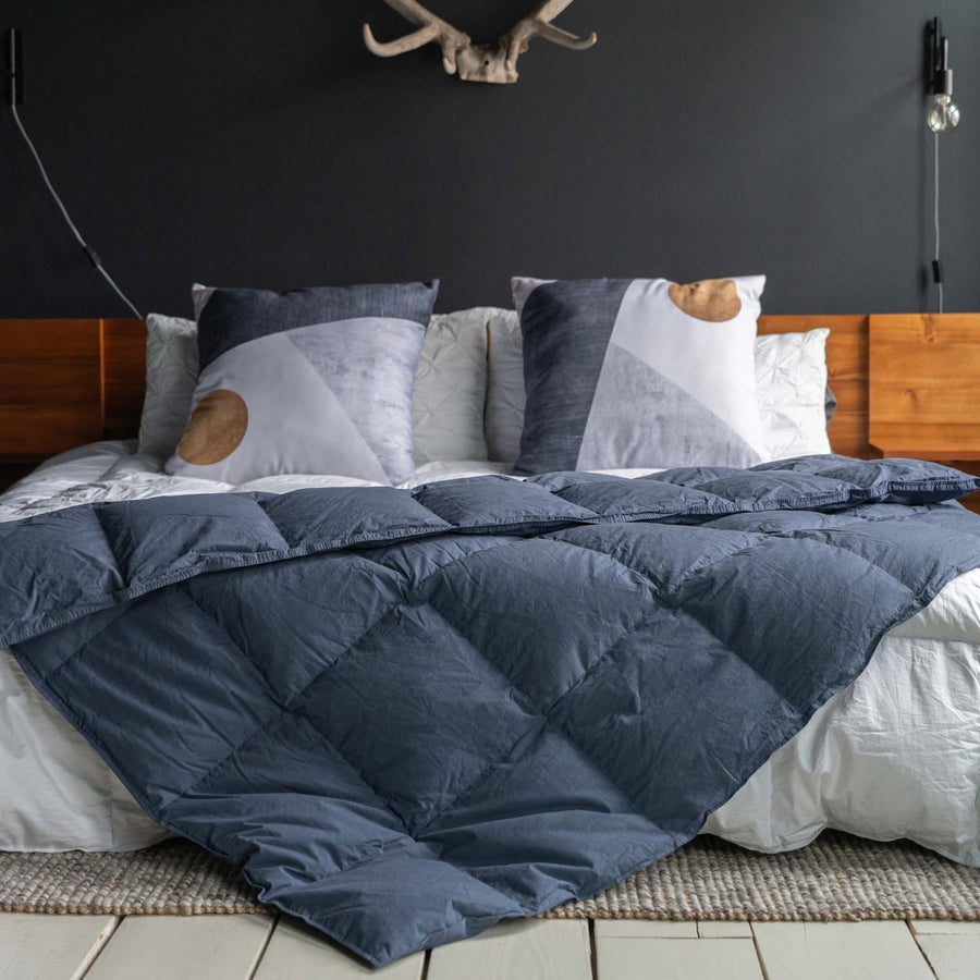Feathered Friends organic down throw Navy blue color on a bed with wood headboard, large pillows, and antlers on the wall