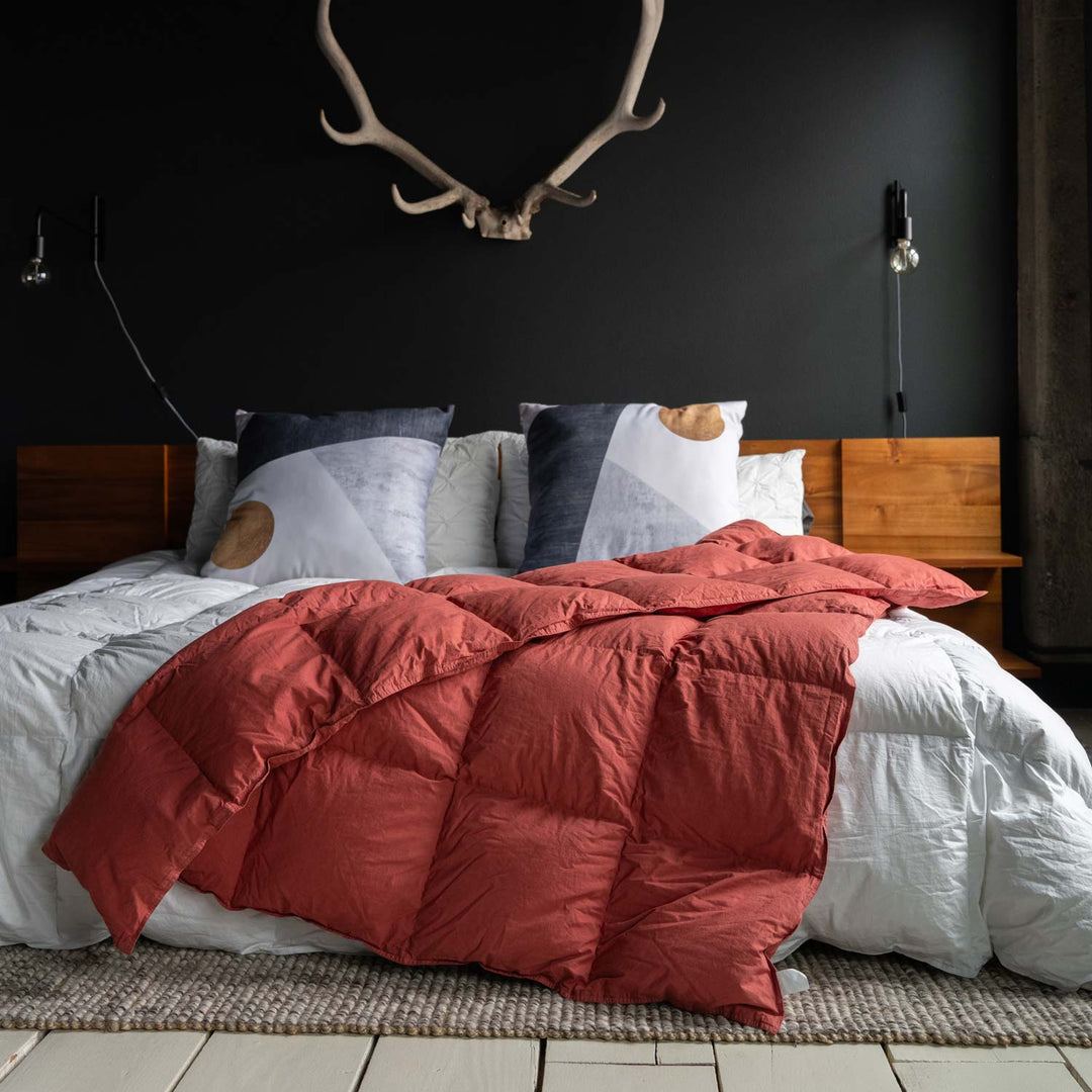 Feathered Friends organic down throw Rose red color on a bed with wood headboard, large pillows, and antlers on the wall