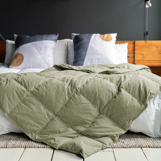 Feathered Friends organic down throw Sage green color on a bed with wood headboard and large pillows