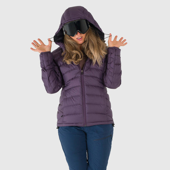 Studio front hood toggle detail view of a woman with goggles on wearing a dusky purple Women's Feathered Friends Eos Down Jacket