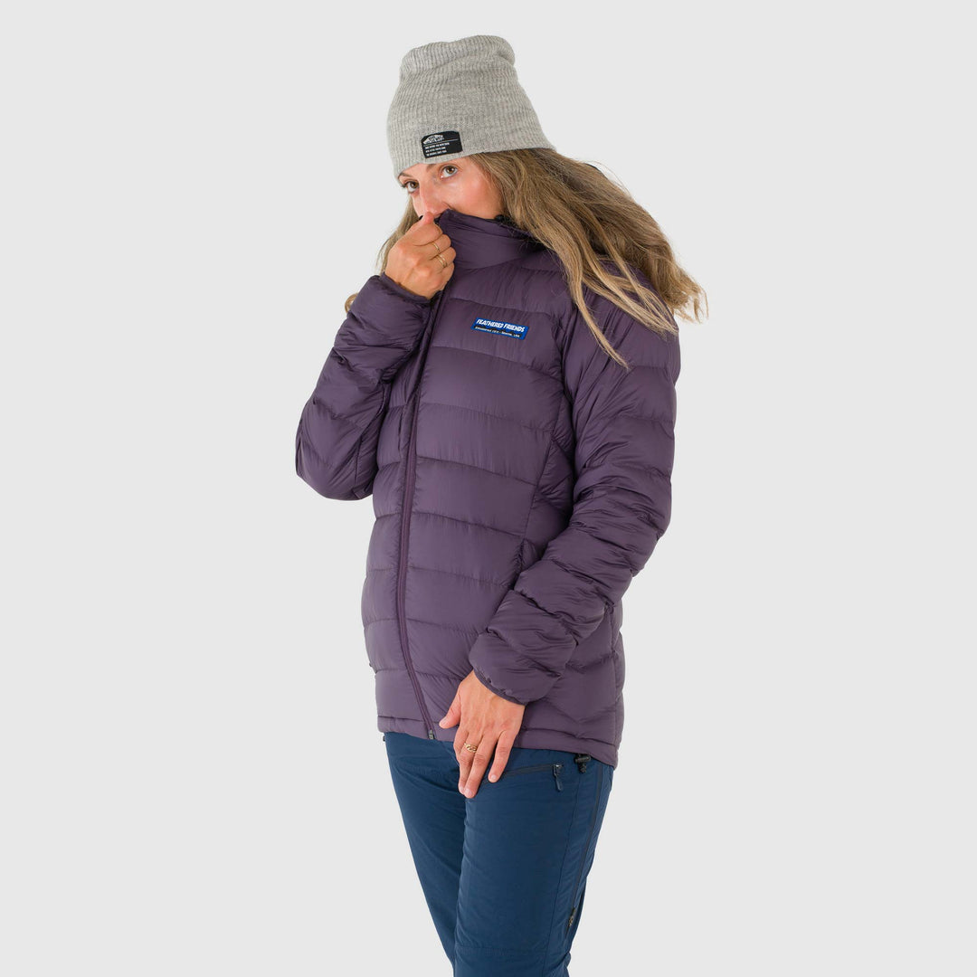 Studio front view of woman wearing a zipped up dusky purple Women's Feathered Friends Eos Down Jacket