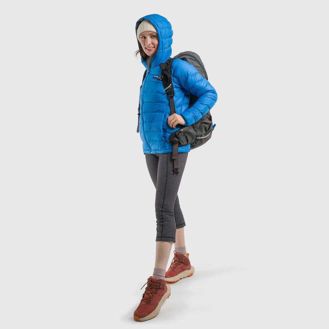 Studio front view of woman wearing a sky blue Women's Feathered Friends Eos Down Jacket with a backpack