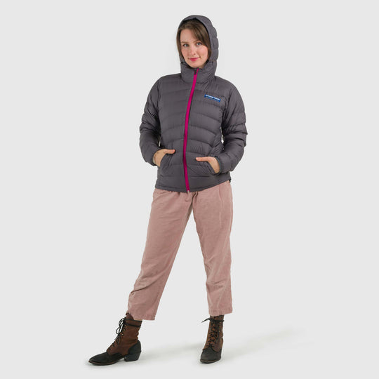 Studio front view of a woman wearing a steel gray Women's Feathered Friends Eos Down Jacket with the hood up
