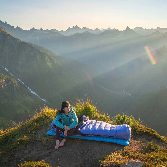 Woman sitting on Feathered Friends sleeping bag at camp high up in the North Cascades