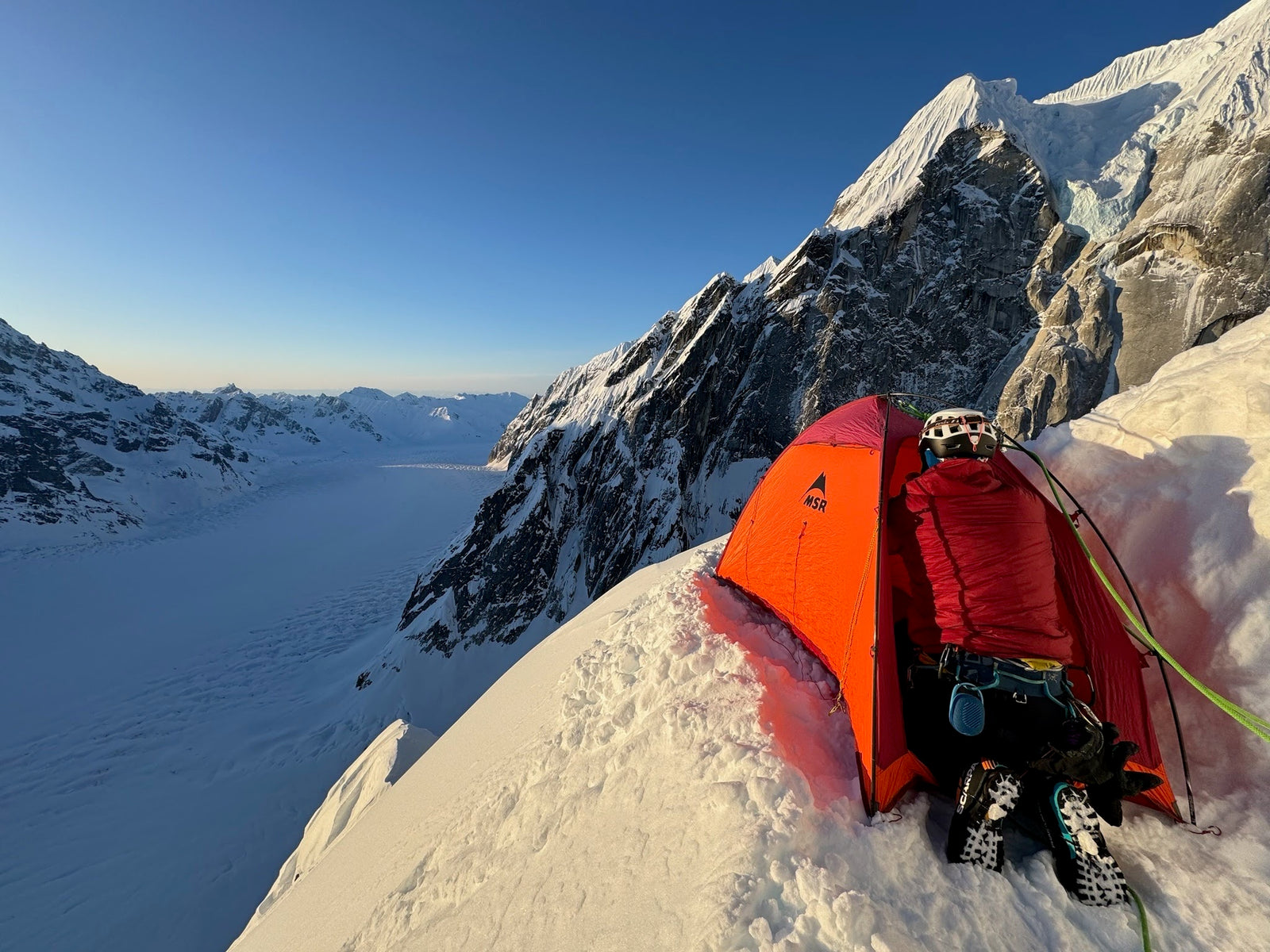 Pictured: Person in climbing gear setting up tent up high in the Alaska range. 
