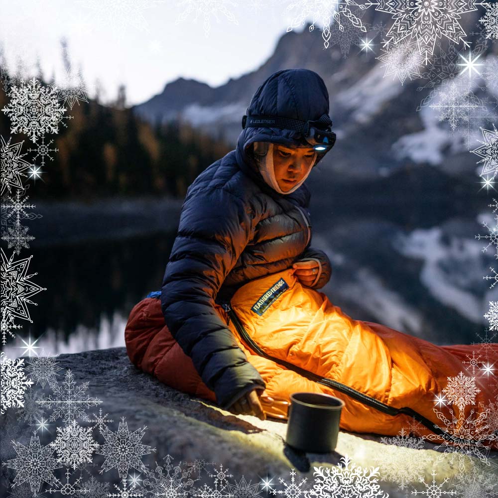 A woman sitting in a Feathered Friends Egret UL in the evening with a border of snowflakes