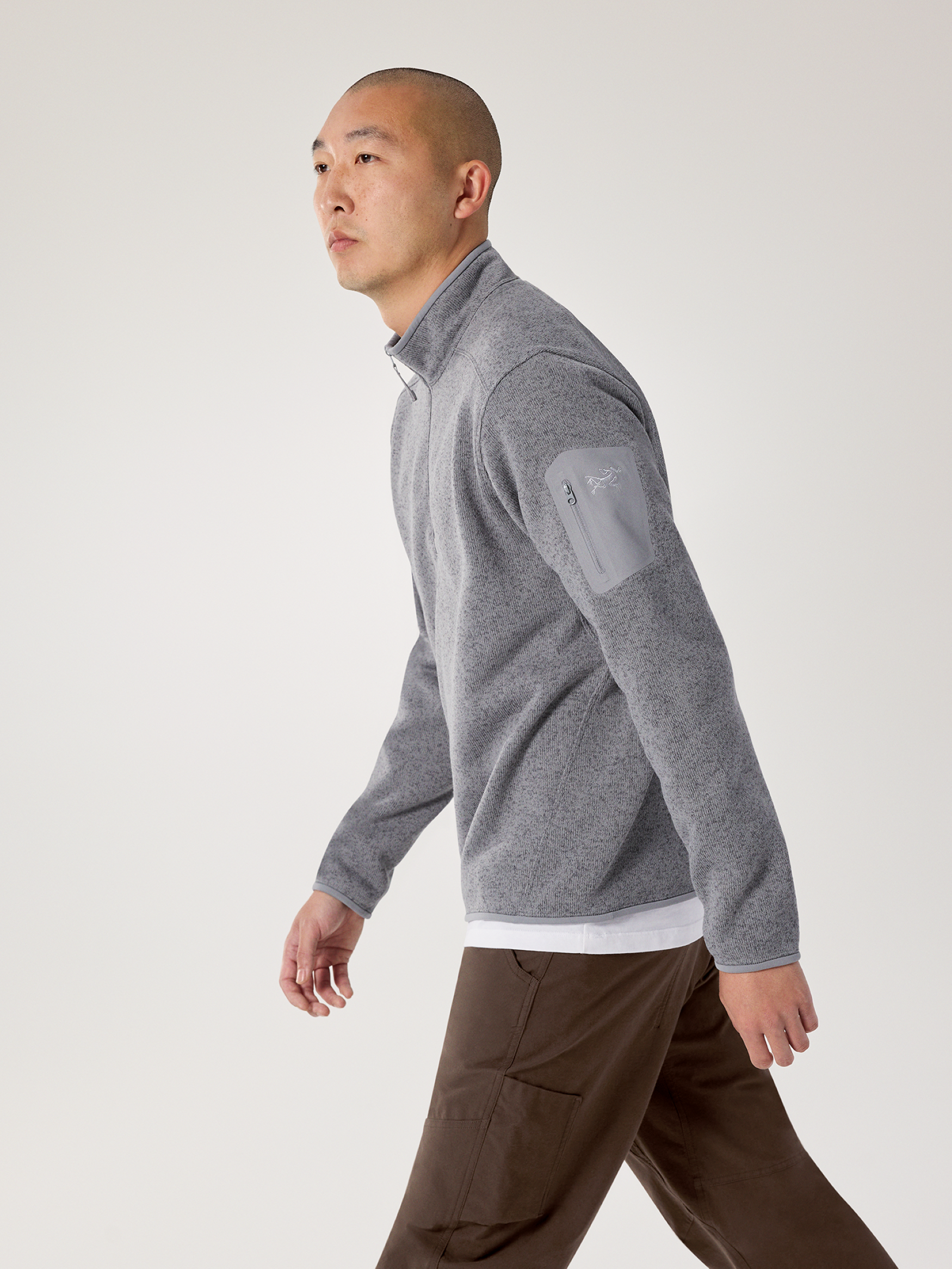 Man wearing Cloud Heather Arc'teryx Covert zip-up sweater and brown pants on a white background