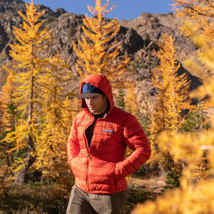 Person wearing Rorange (red) Eos Down Jacket in a grove of golden larches in the Cascades