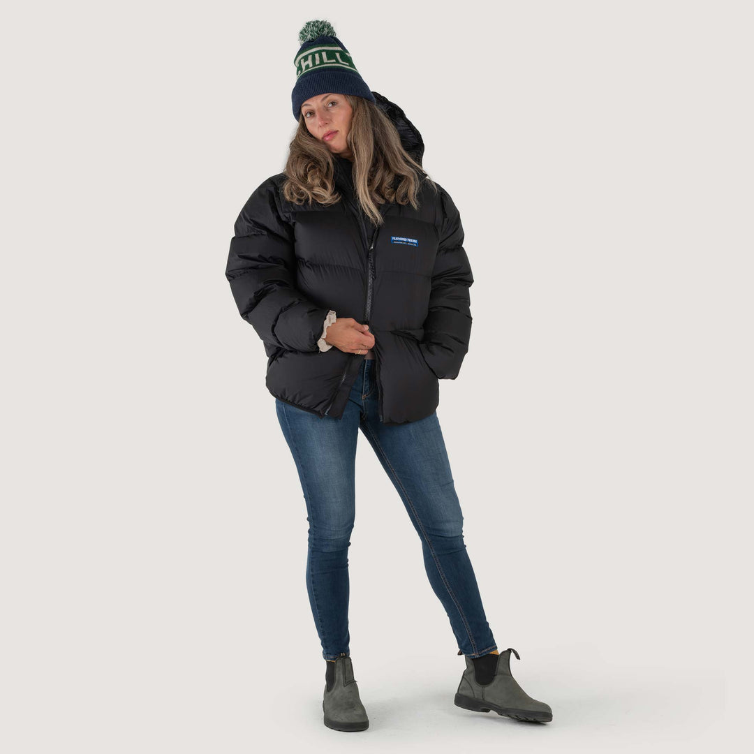 Studio front view of a woman wearing a black Feathered Friends Hooded Helios down puffer jacket