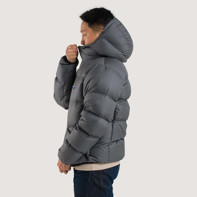 Studio side view of a man wearing a cinder gray Feathered Friends Hooded Helios down puffer jacket