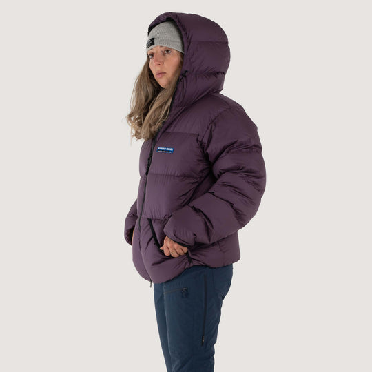 Studio front view of a woman wearing a nightshade purple Feathered Friends Hooded Helios down puffer jacket