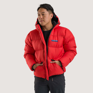 Studio front view of a man wearing a poppy red Feathered Friends Hooded Helios down puffer jacket