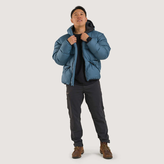 Studio front view of a man wearing a slate blue Feathered Friends Hooded Helios down puffer jacket