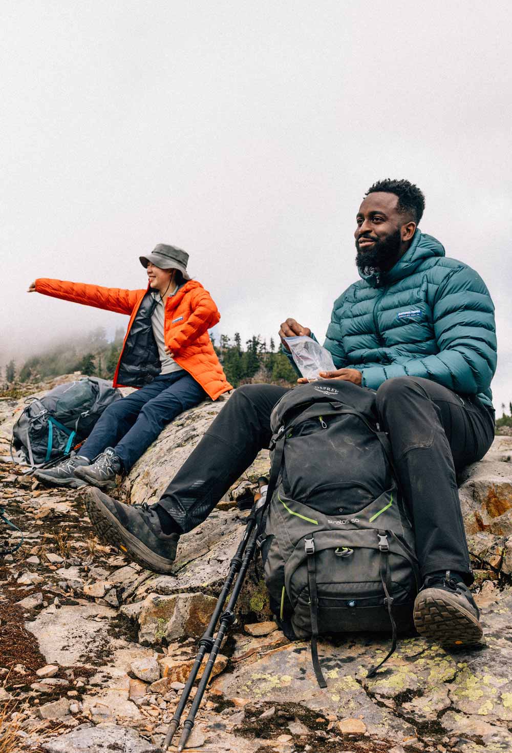 A woman and a man at a backpacking rest break wearing Feathered Friends Eos jackets