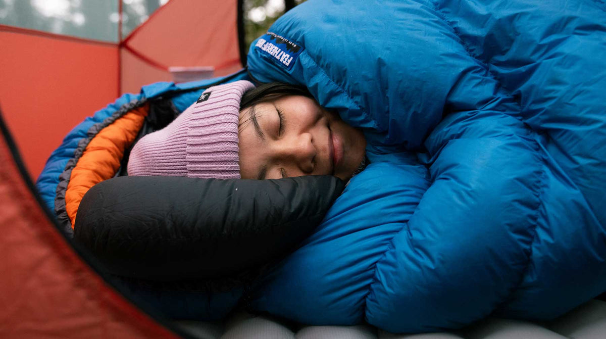 A camper resting in a blue Feathered Friends down sleeping bag inside a tent