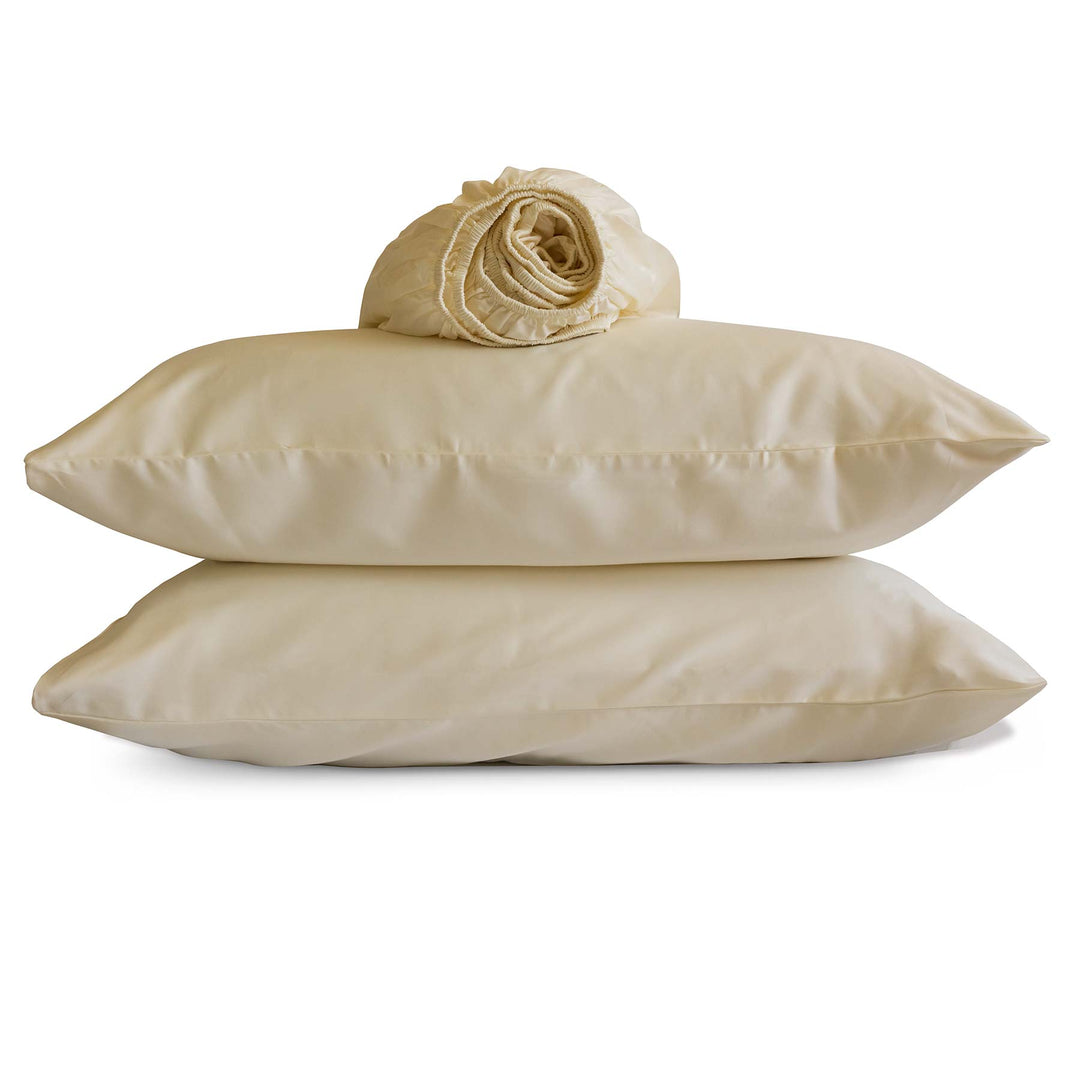 Studio photo of Ivory-color Feathered Friends Organic Cotton rolled Fitted Sheet and two pillow cases