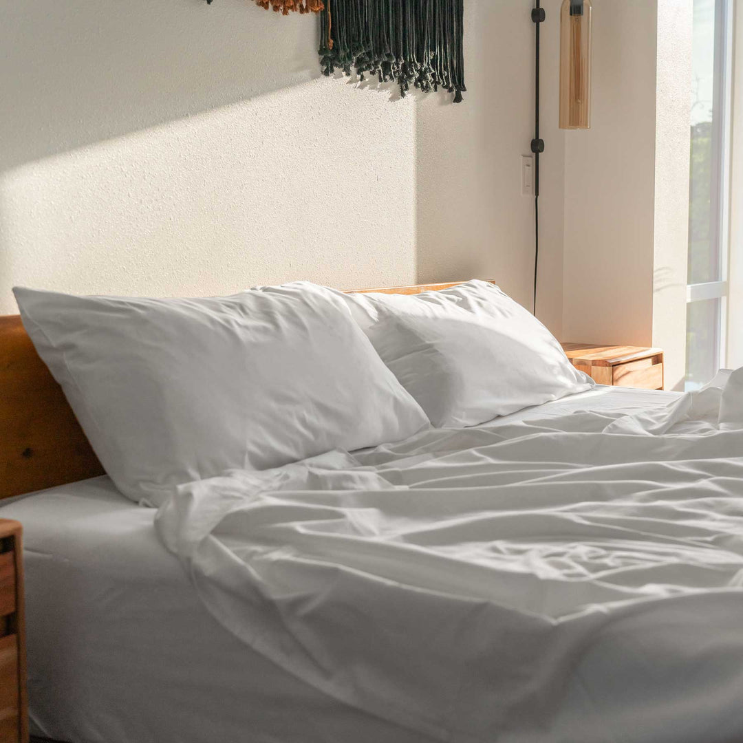 Two White Feathered Friends Organic Cotton Pillow Cases on a bed with a wood headboard