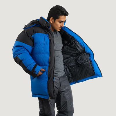 A model wearing the Feathered Friends Rock and Ice Expedition Parka in blue, showing the interior pockets and details