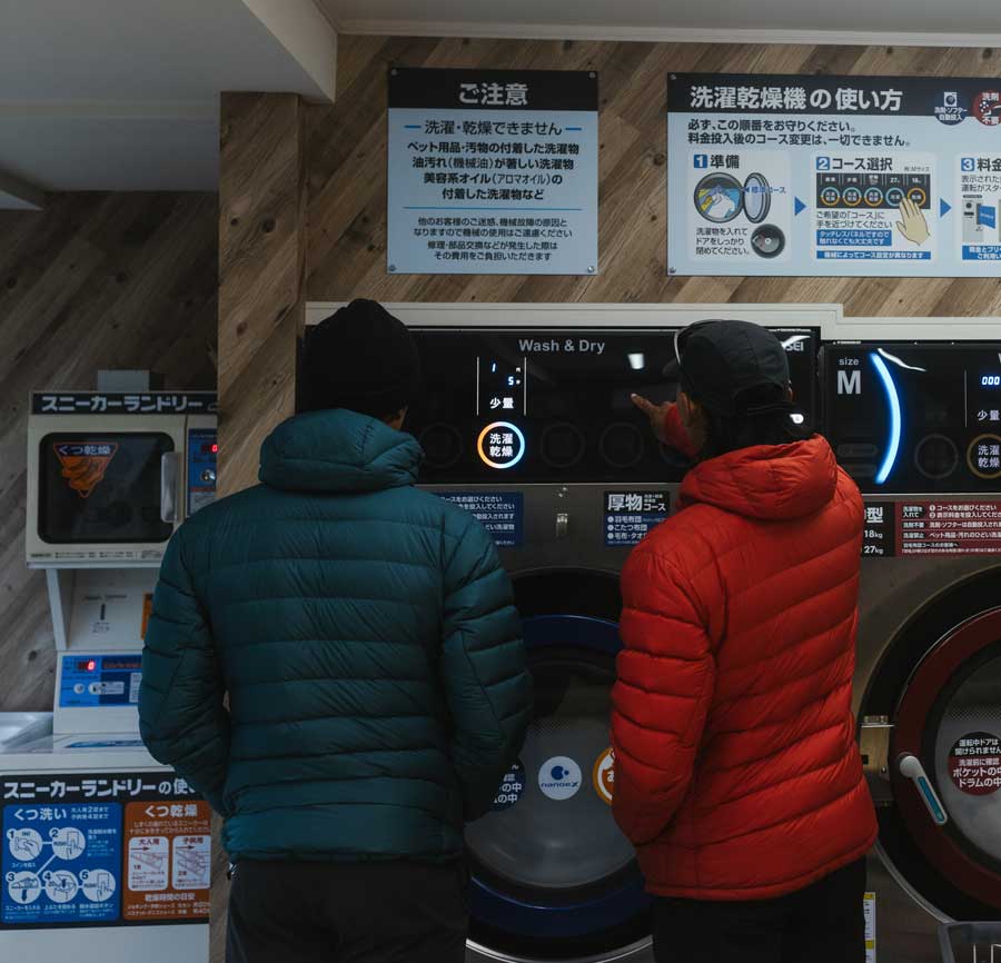 Two people in Eos jackets at a laundromat in Japan with instructions on the wall.