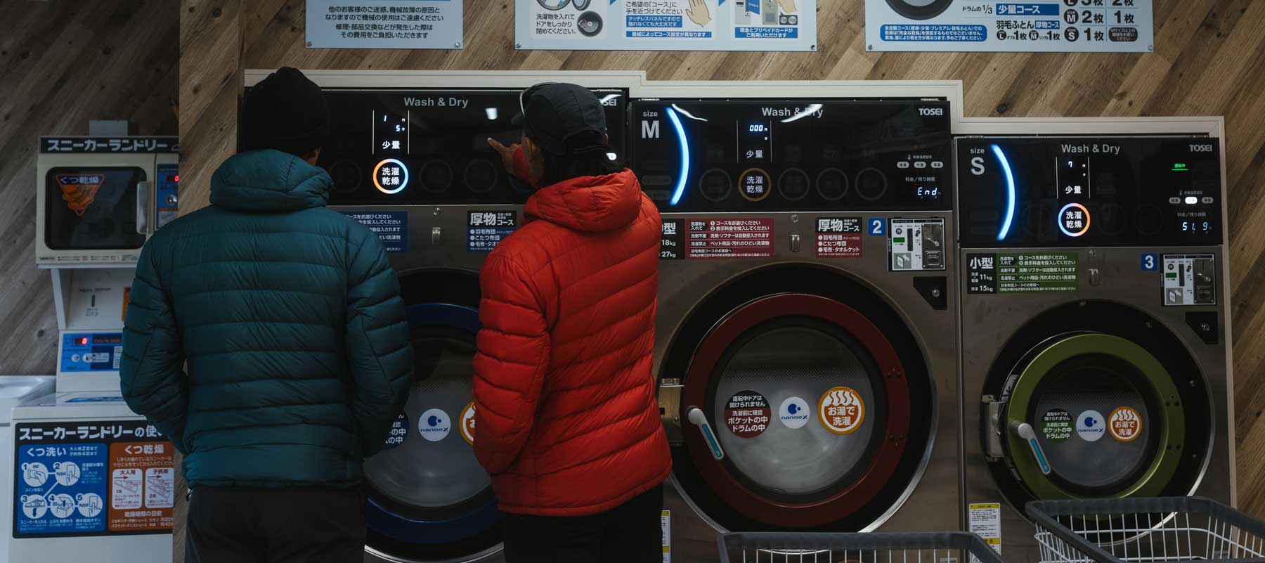 Two people in Eos jackets at a laundromat in Japan with instructions on the wall.