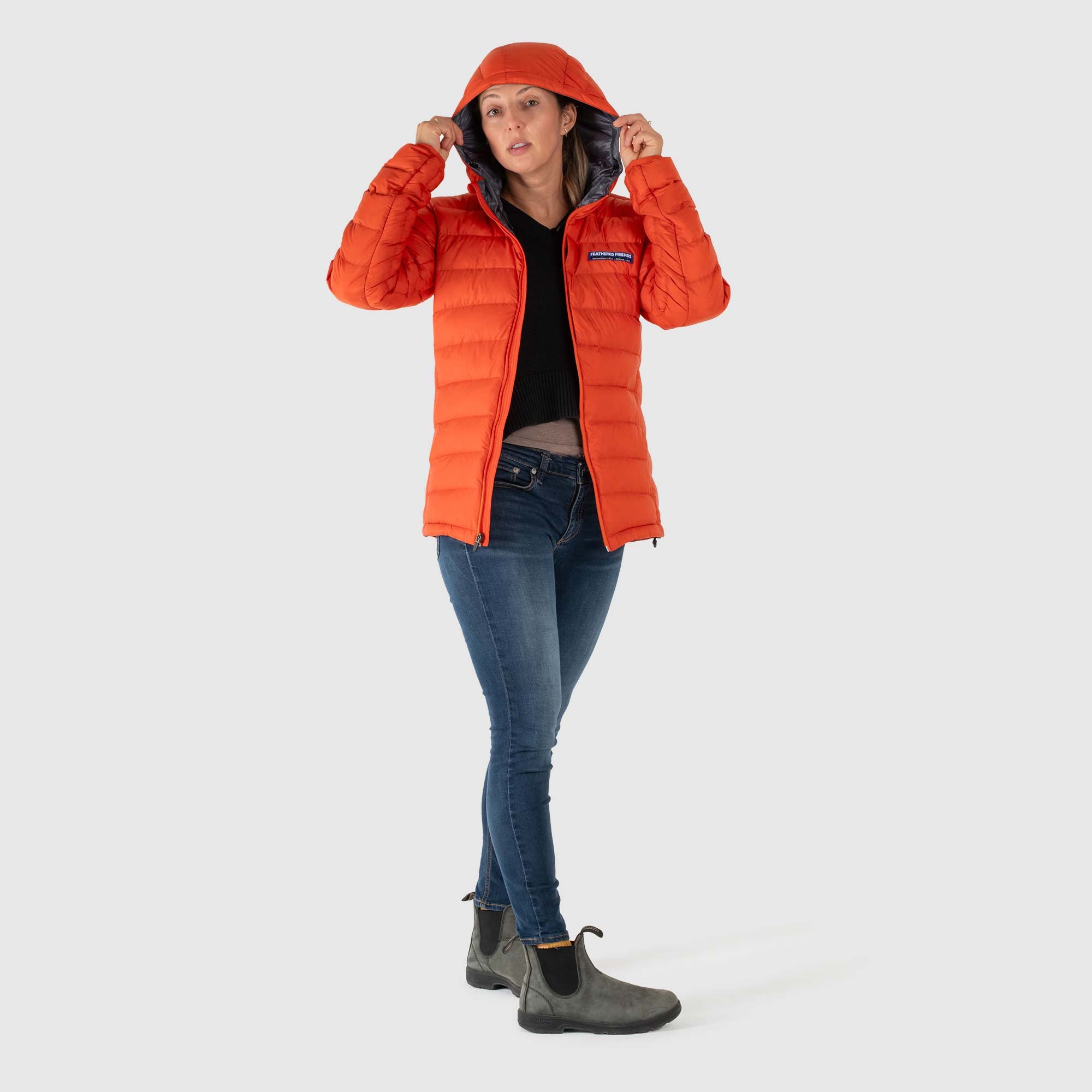 Studio front view of woman wearing a rorange Women's Feathered Friends Eos Down Jacket